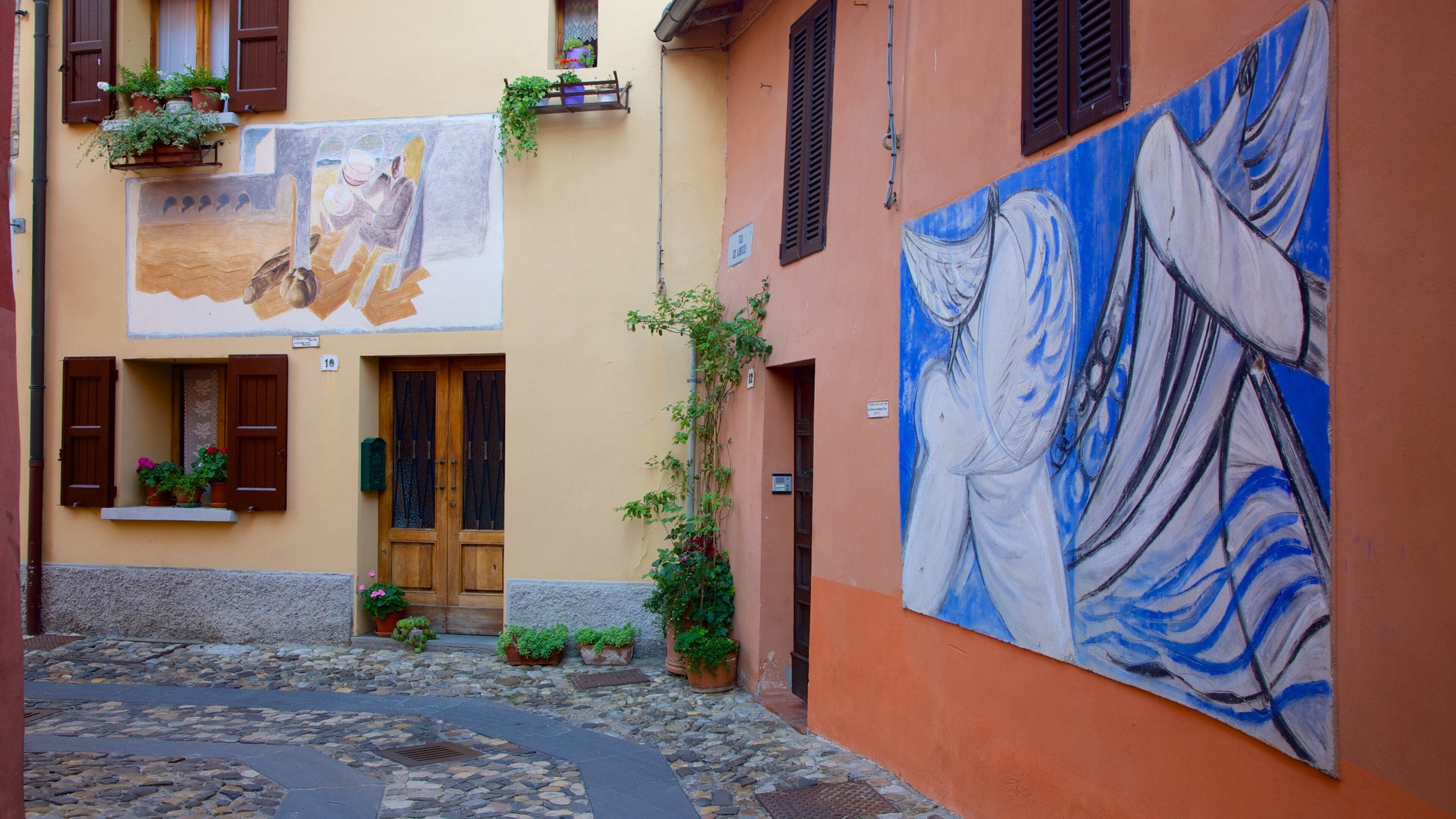 A narrow cobblestone street with a building featuring a large mural and potted plants.