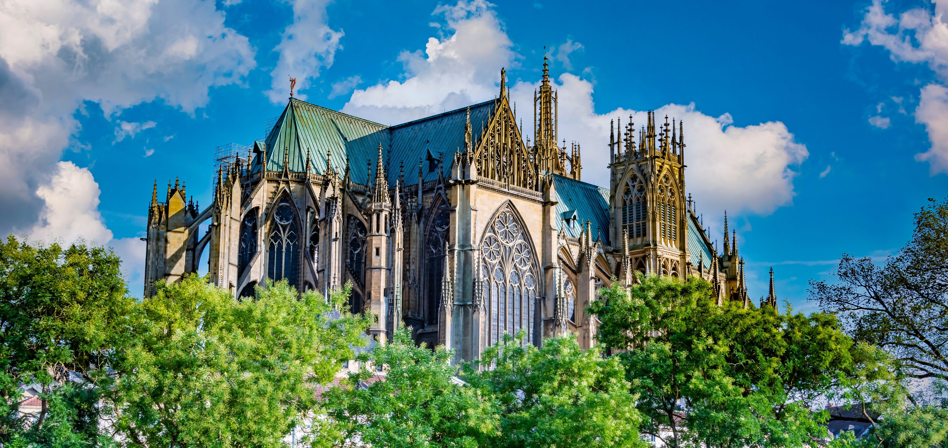A Gothic cathedral with intricate spires and a green roof, surrounded by lush green trees.