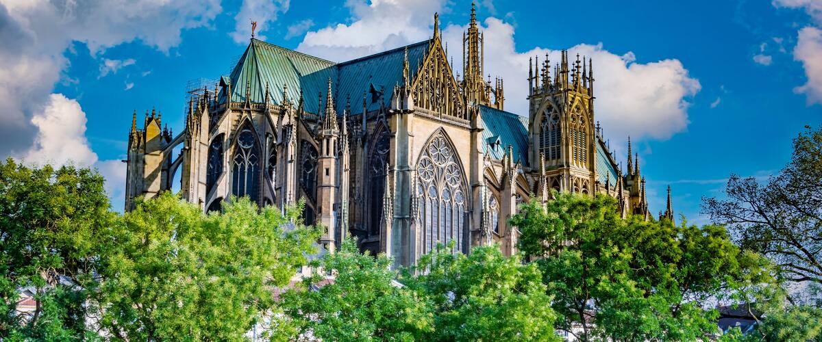 A Gothic cathedral with intricate spires and a green roof, surrounded by lush green trees.