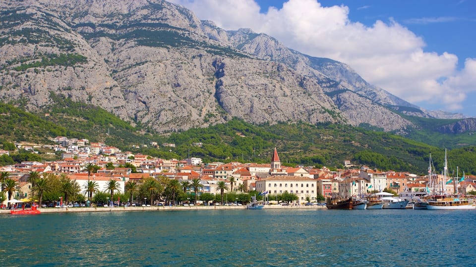 A coastal town with a prominent church, boats, and a mountainous backdrop.