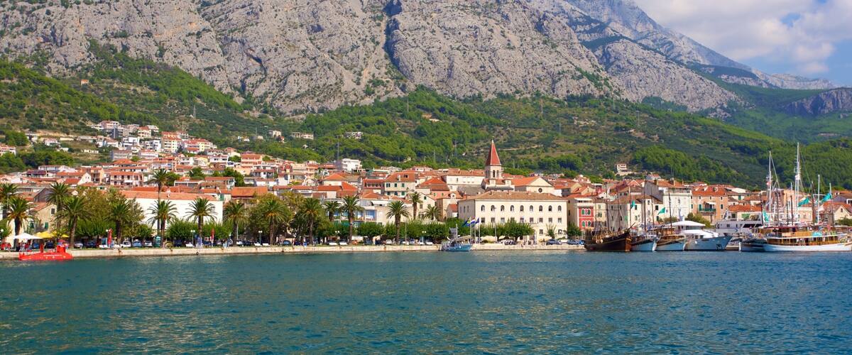 A coastal town with a prominent church, boats, and a mountainous backdrop.