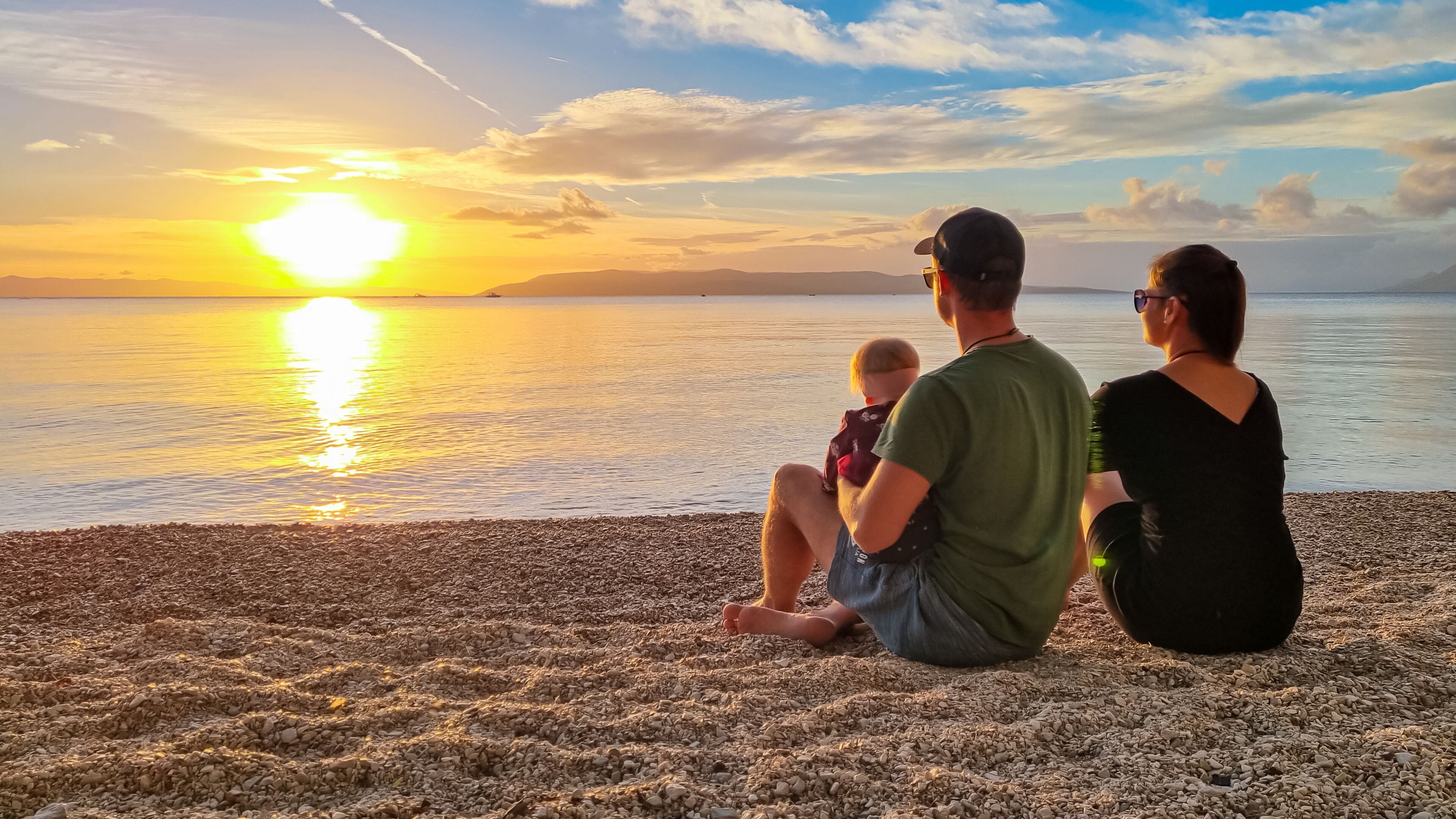 Family with small child enjoying romantic sunset at beach in town Makarska, Split-Dalmatia, Croatia, Europe. Coastline of Makarska Riviera, Adriatic Sea. Dreamlike atmosphere. Family vacation concept