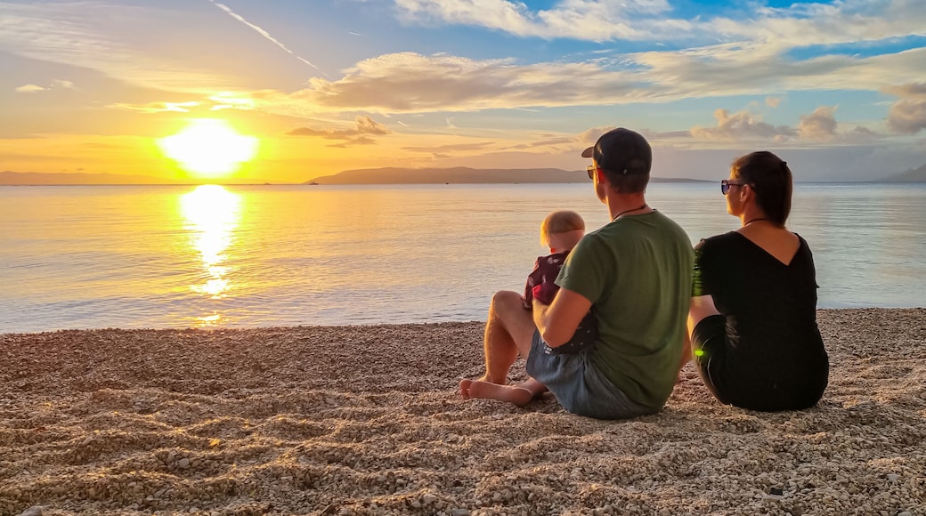 Family with small child enjoying romantic sunset at beach in town Makarska, Split-Dalmatia, Croatia, Europe. Coastline of Makarska Riviera, Adriatic Sea. Dreamlike atmosphere. Family vacation concept