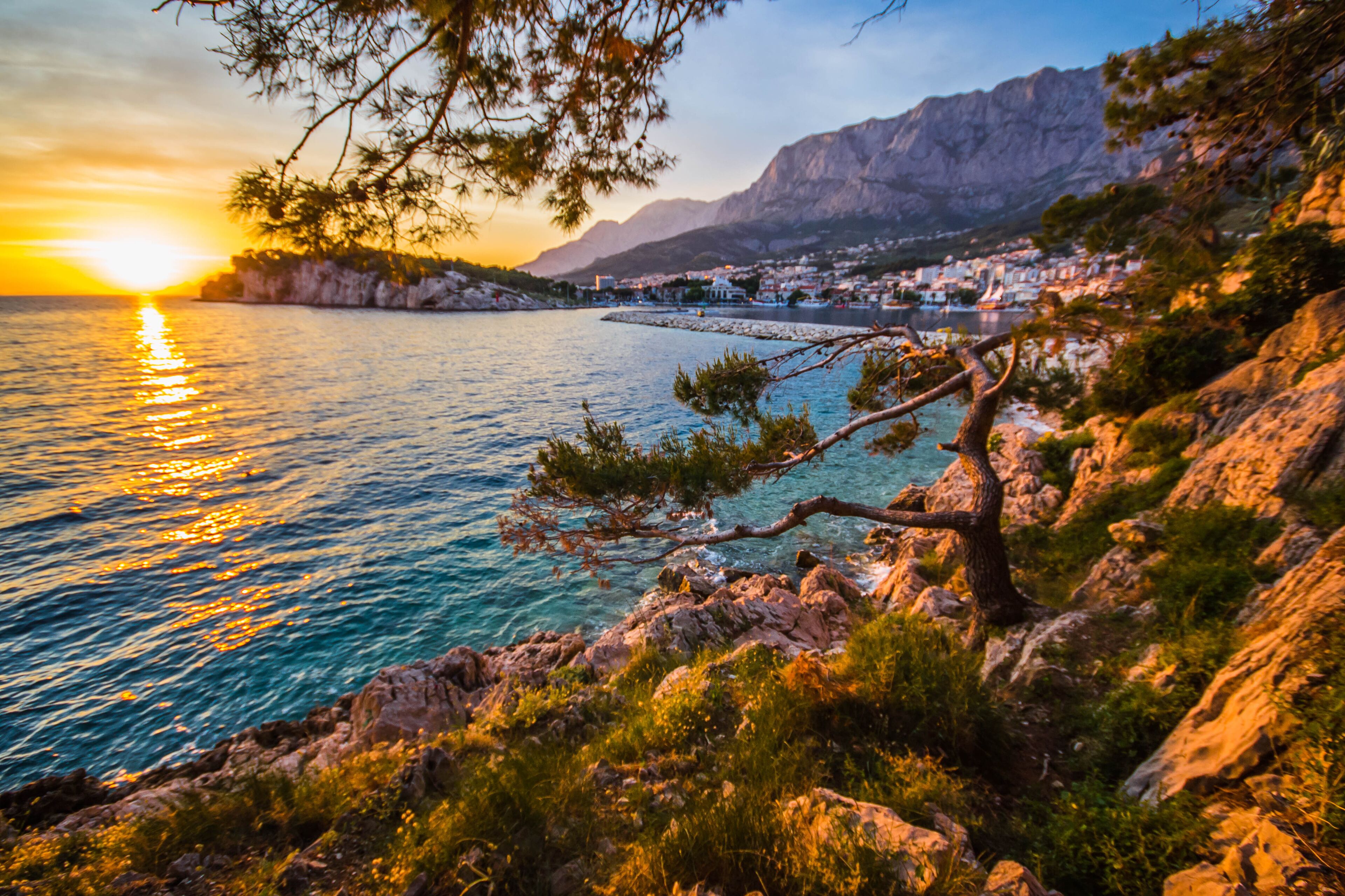 A coastal landscape with a sunset, rocky terrain, and a distant town.