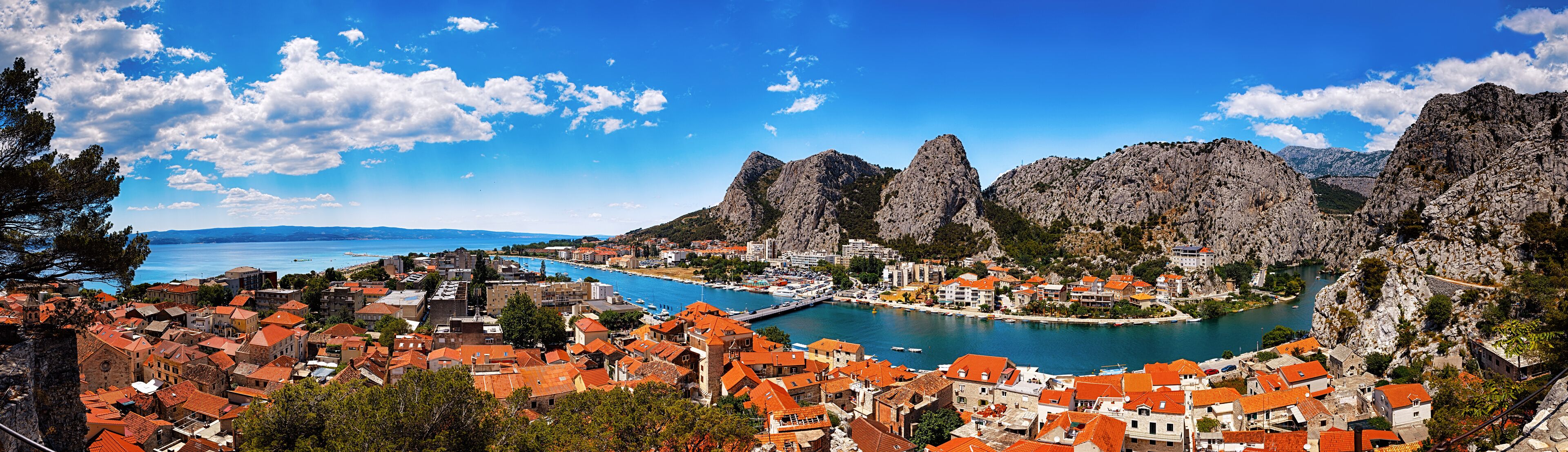 A coastal town with red-roofed buildings, a bay, and rocky mountains.