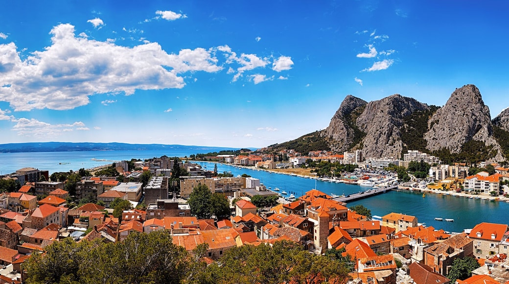 A coastal town with red-roofed buildings, a bay, and rocky mountains.