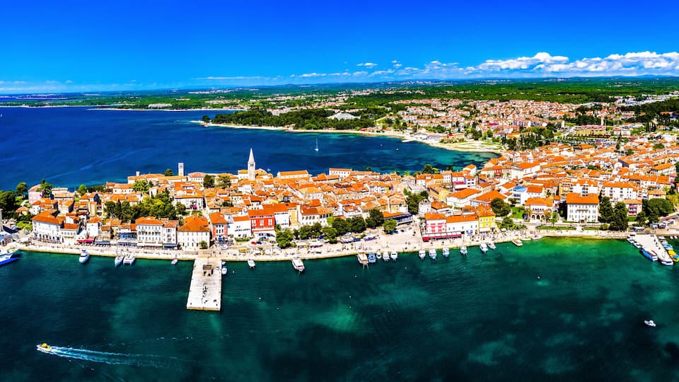 An aerial view of a coastal town with a prominent church, a marina, and surrounding greenery.