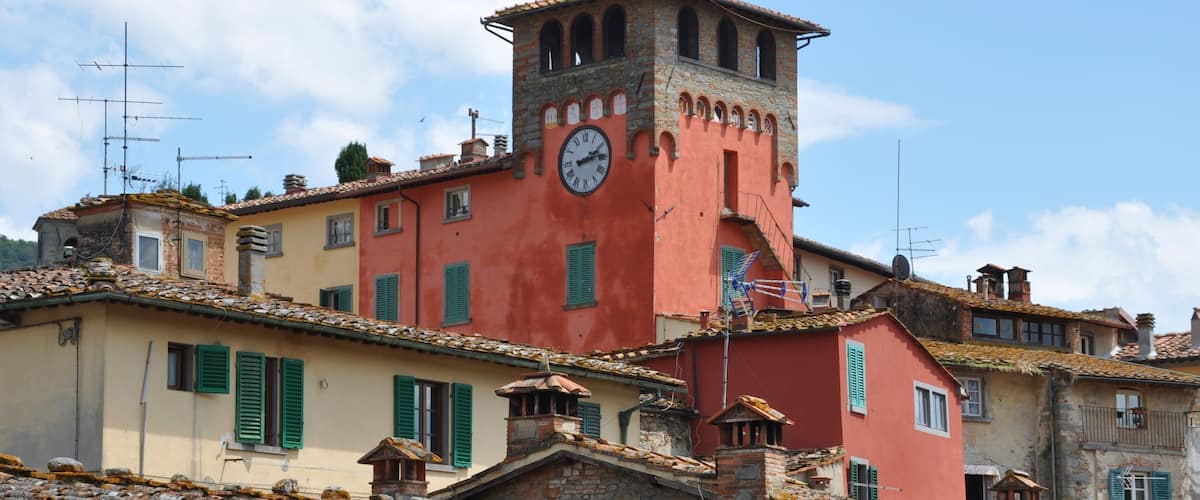 A historic town with colorful buildings, a prominent clock tower, and terracotta-tiled roofs.