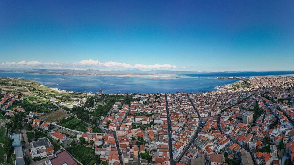 A coastal town with red-roofed buildings, a large body of water, and distant mountains.