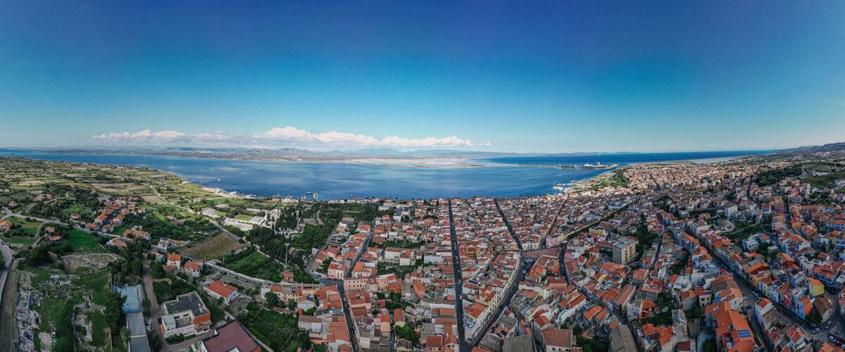 A coastal town with red-roofed buildings, a large body of water, and distant mountains.