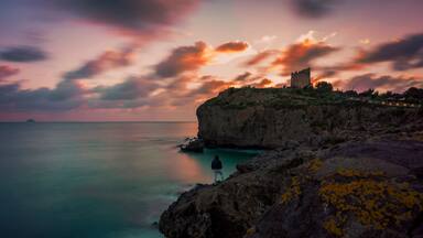 A coastal landscape with a cliff, a person standing on the edge, and a castle on top.