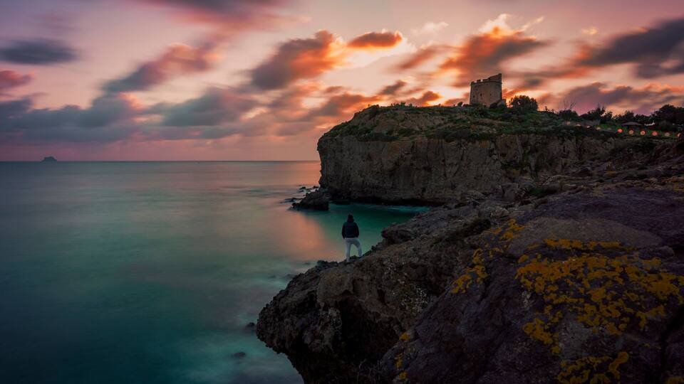 A coastal landscape with a cliff, a person standing on the edge, and a castle on top.