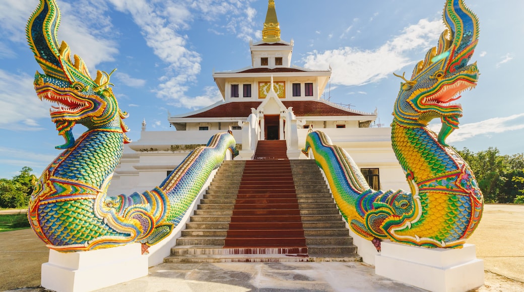 A pair of colorful Naga statues stand majestically atop the grand staircase of Wat Pha Tak Suea Temple in Sangkhom District, Nong Khai Province, Thailand, against a clear blue sky.