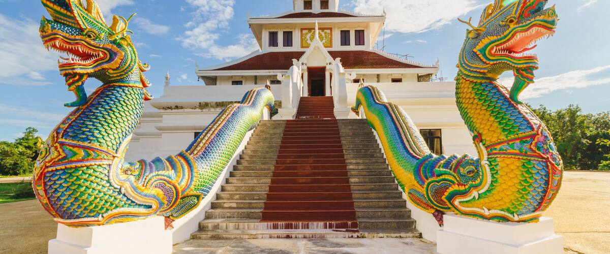 A temple with a golden spire, two colorful dragon statues, and a red staircase leading to the entrance.