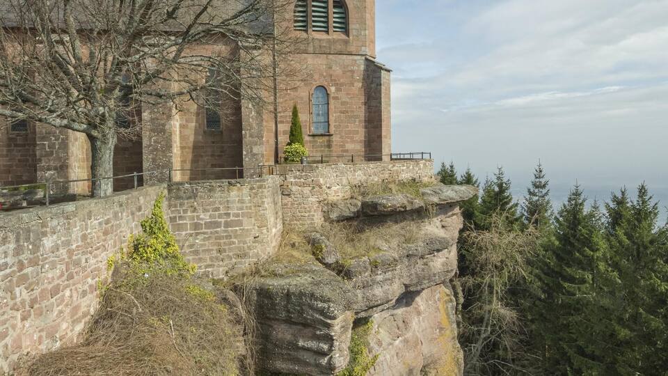 A historic church perched on a rocky cliff with a clear view of the surrounding forest.