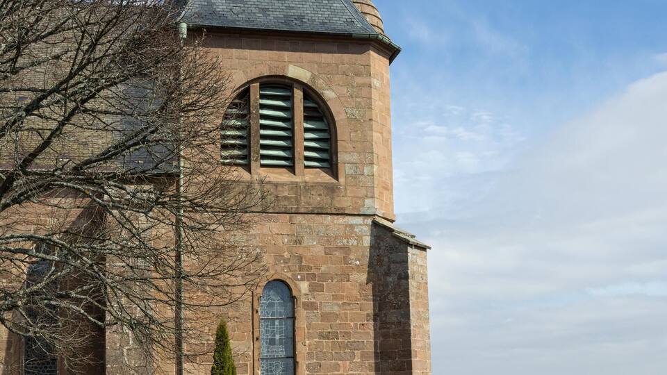 A historic church with a bell tower, stone walls, and a statue on top.