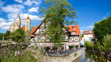 A riverside town with traditional half-timbered houses, a church with a tall tower, and a bridge.
