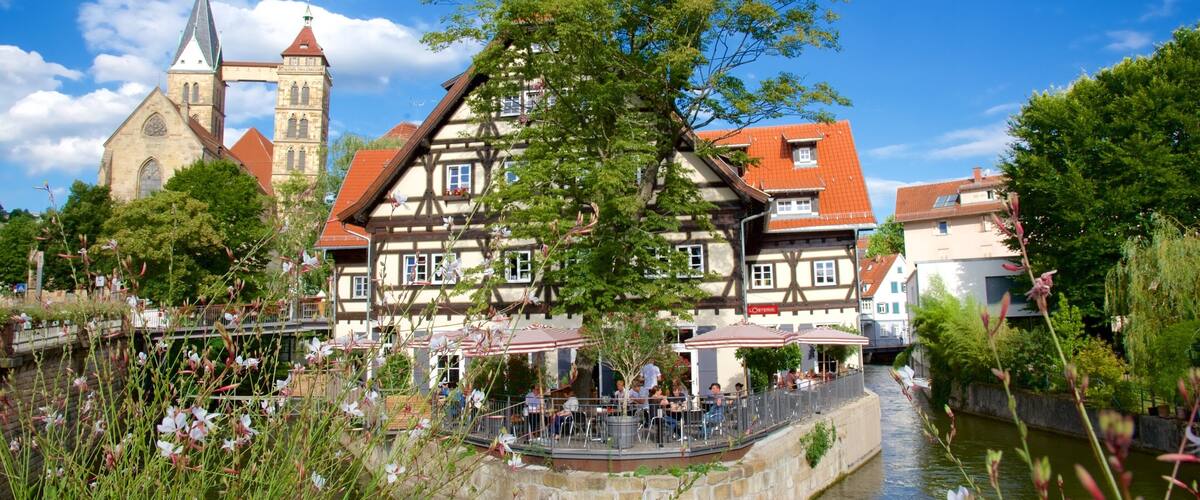 A riverside town with traditional half-timbered houses, a church with a tall tower, and a bridge.