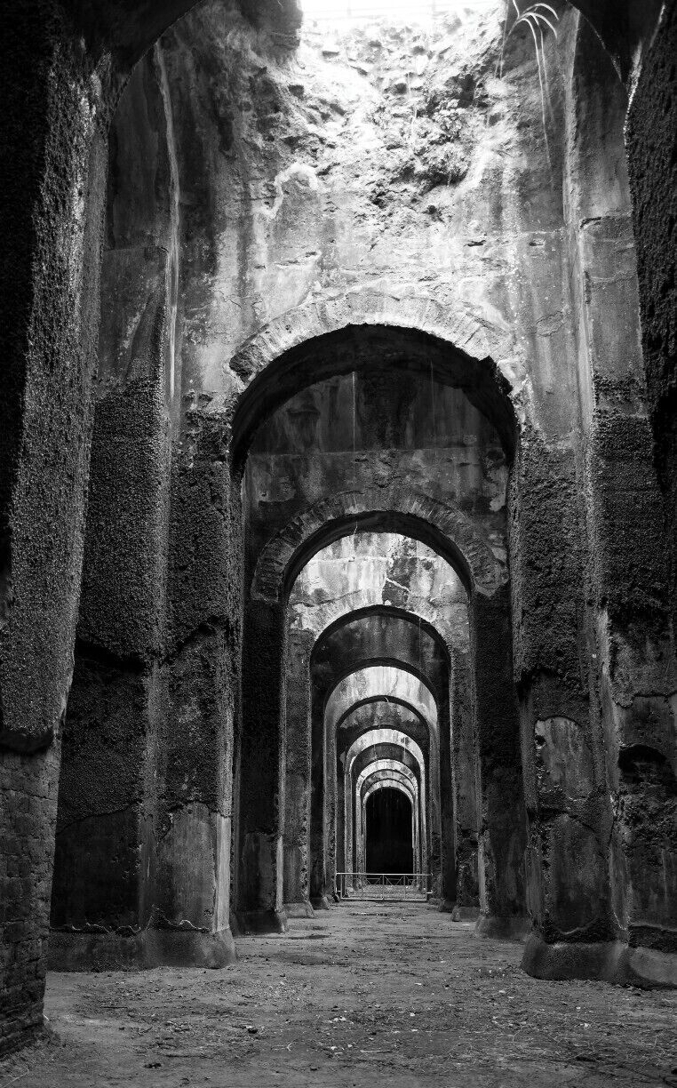 An arched stone corridor with moss-covered columns, leading to a dark doorway.