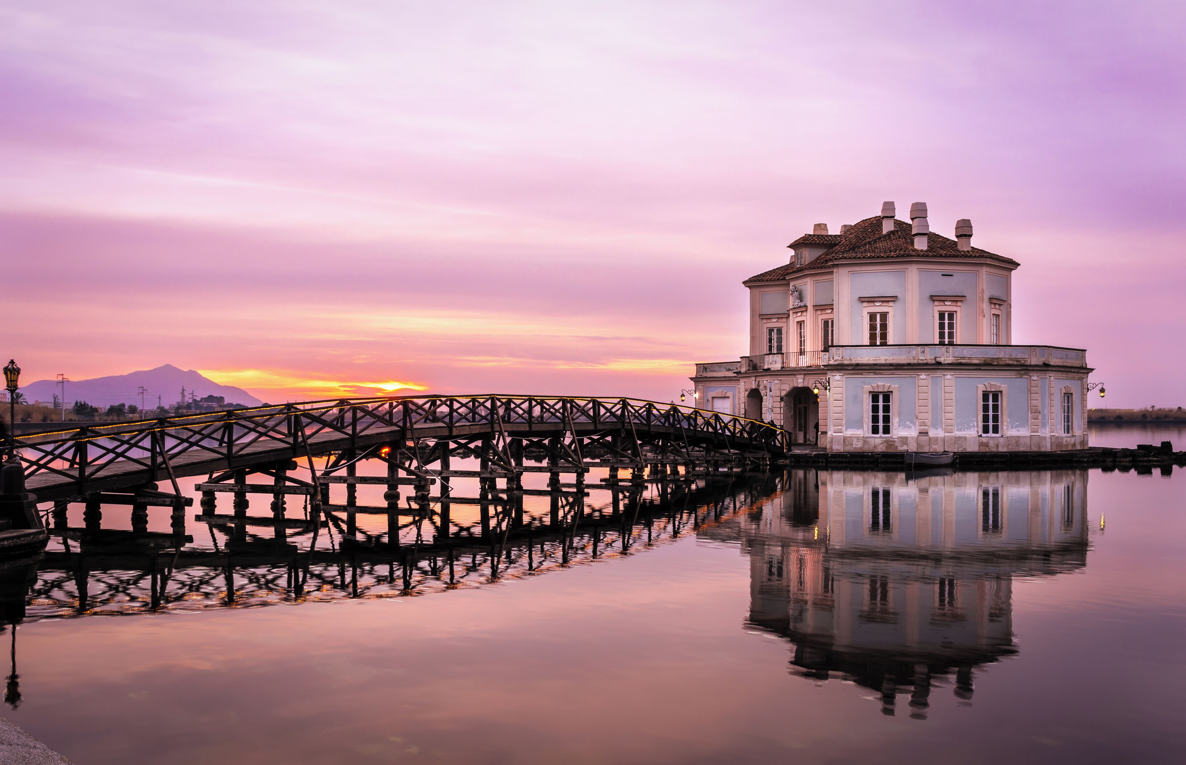 A historic building with a round tower, a wooden bridge, and a mountain in the background.