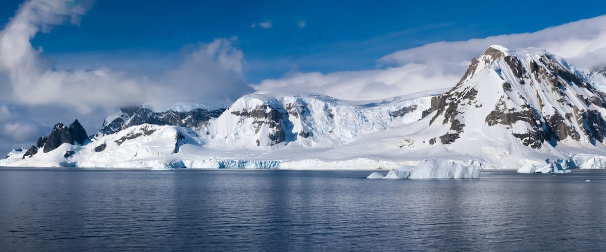A glacier with icebergs and a mountain range under a clear sky.