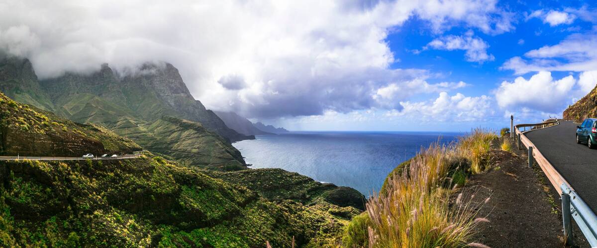 A coastal road with a guardrail, lush green hills, and a view of the ocean.