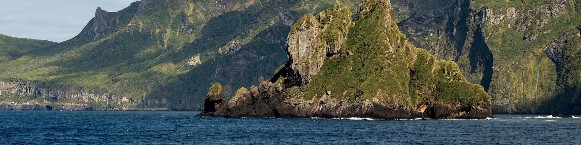 A rugged island with steep cliffs and a small waterfall in the background.