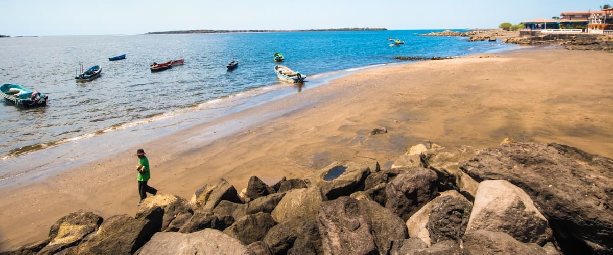 A beach with boats, rocks, and a clear sky.