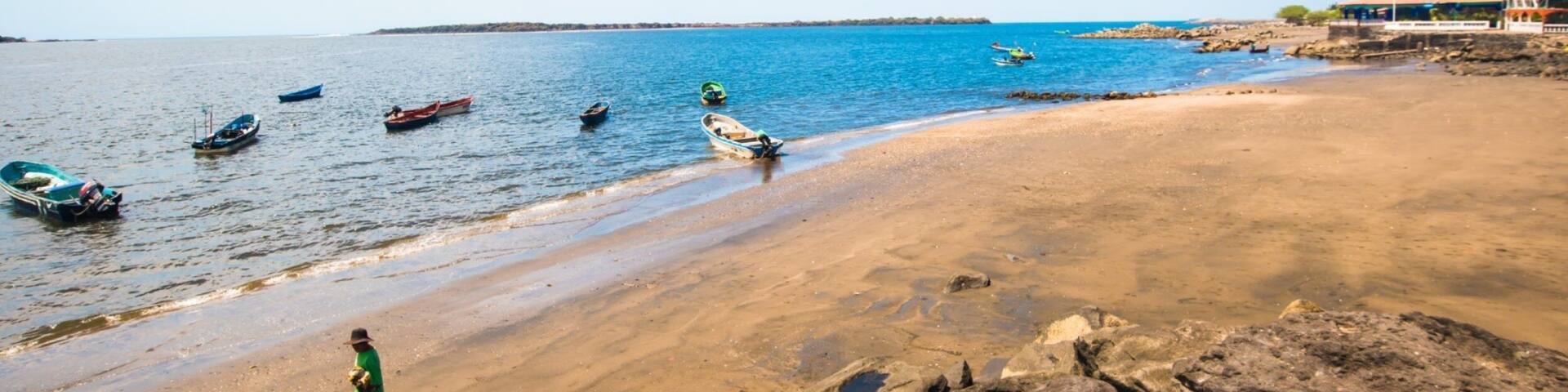A beach with boats, rocks, and a clear sky.
