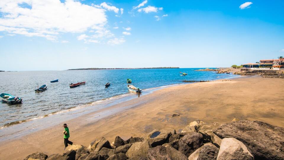 A beach with boats, rocks, and a clear sky.