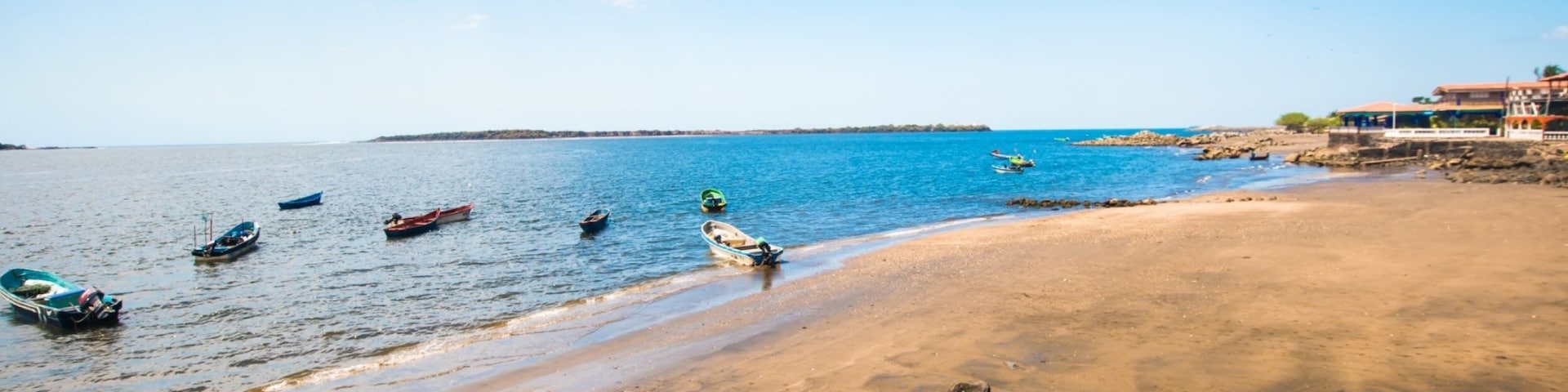 Una playa con barcos, rocas y cielo despejado.