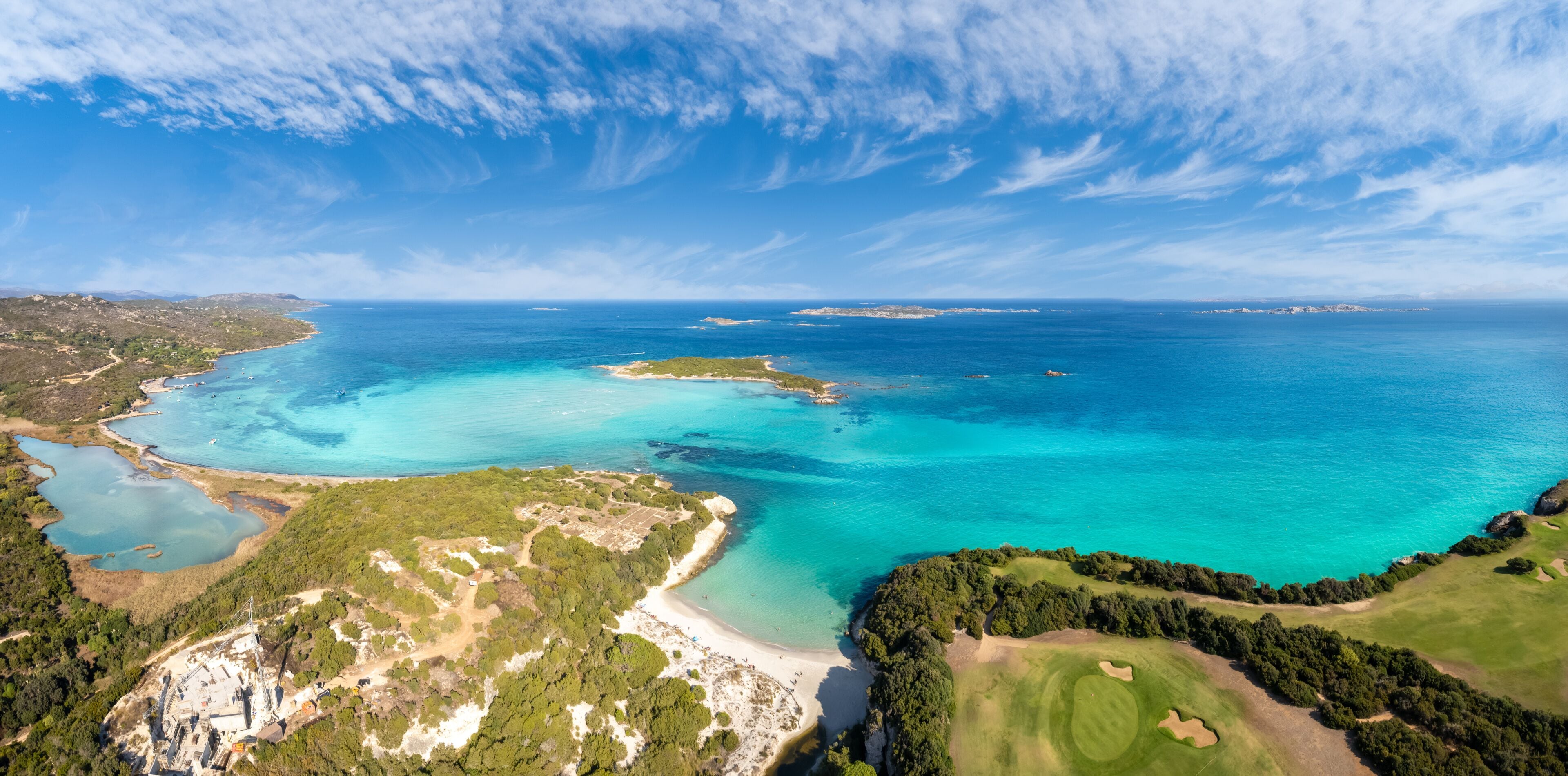 Un paisaje costero con aguas turquesas cristalinas, una playa arenosa y un campo de golf.