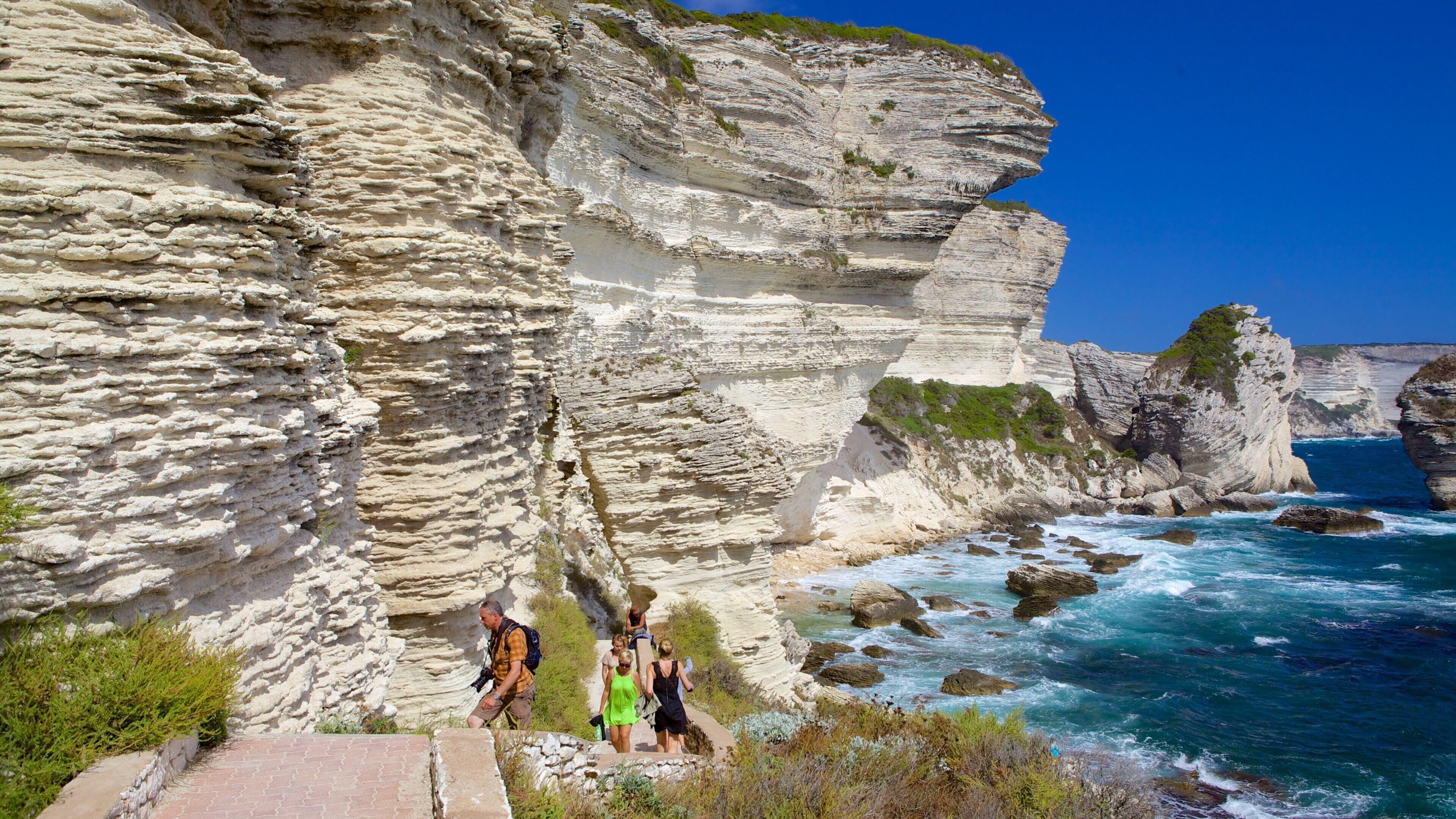A coastal cliff with layered rock formations and a path leading down to the sea.