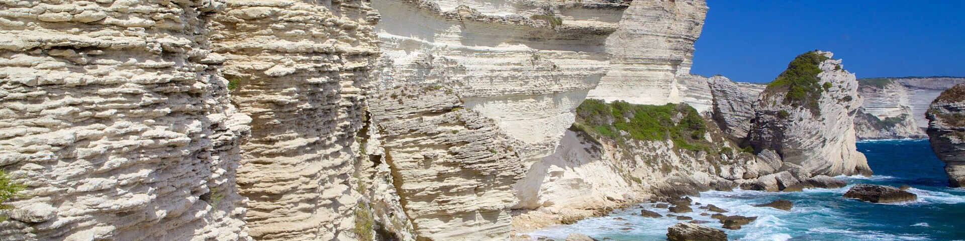 A coastal cliff with layered rock formations and a path leading down to the sea.