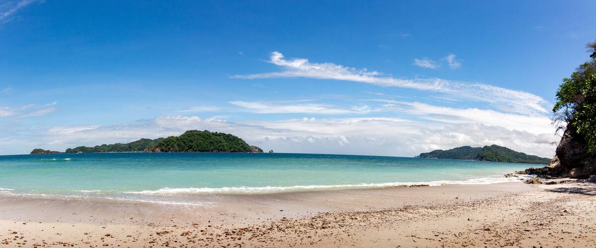A beach with clear turquoise water, a sandy shore, and a small island with lush greenery in the distance.