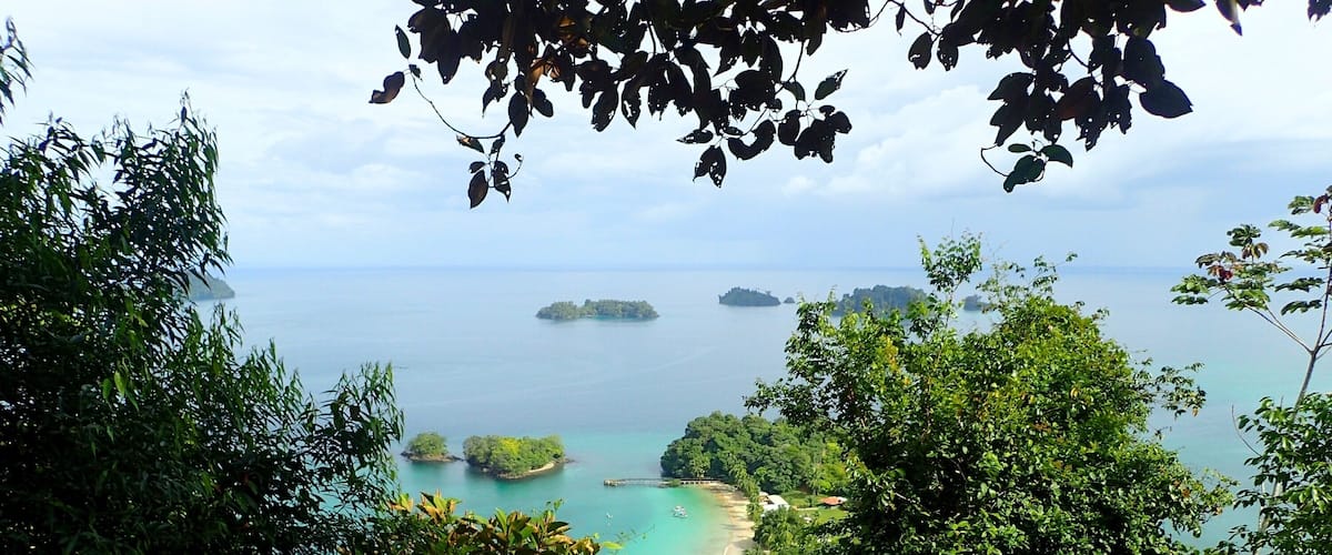 A coastal landscape with dense foliage, a beach, and several small islands in the distance.