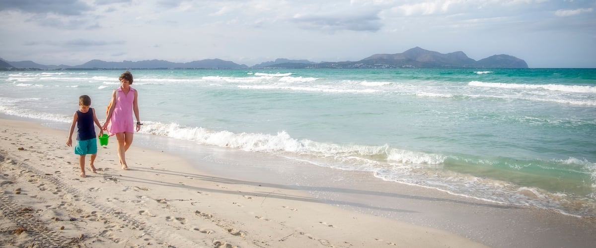 A beach with waves, a clear sky, and distant mountains.