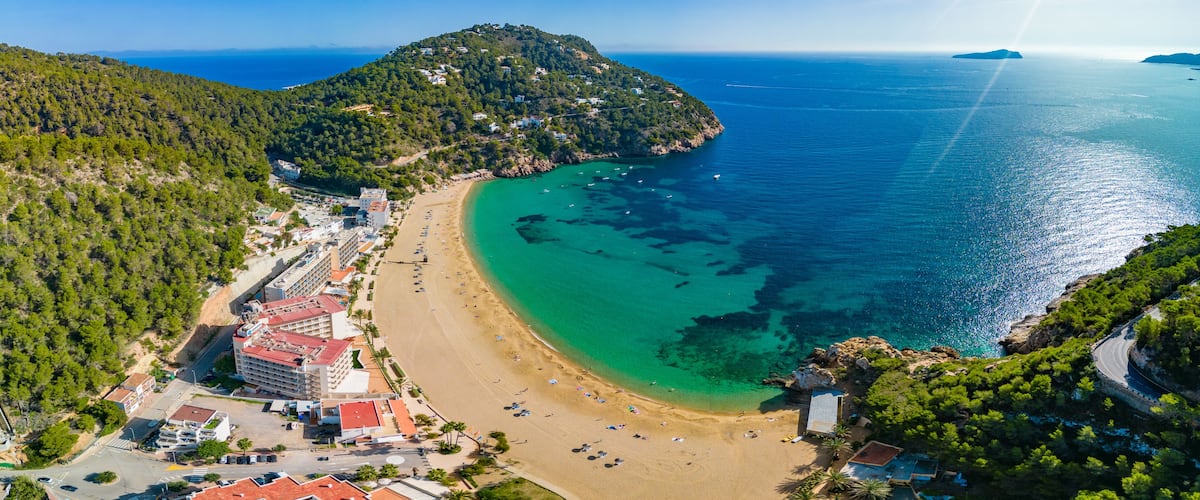 A coastal town with a beach, buildings, and a mountainous backdrop.