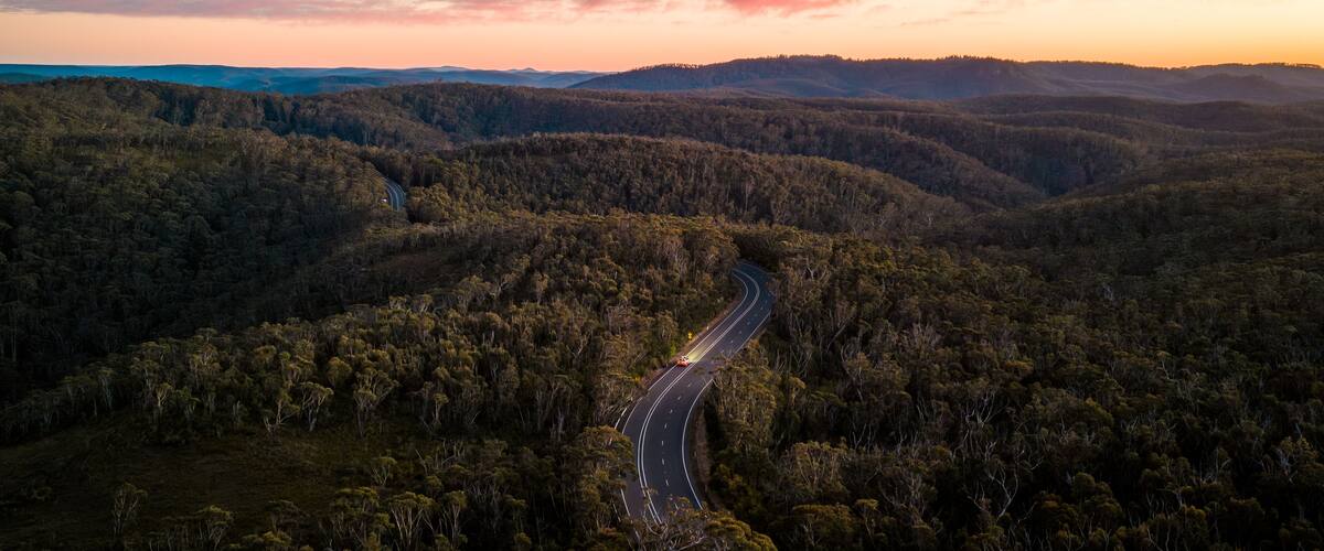 A winding road through a forested valley with a sunset in the background.