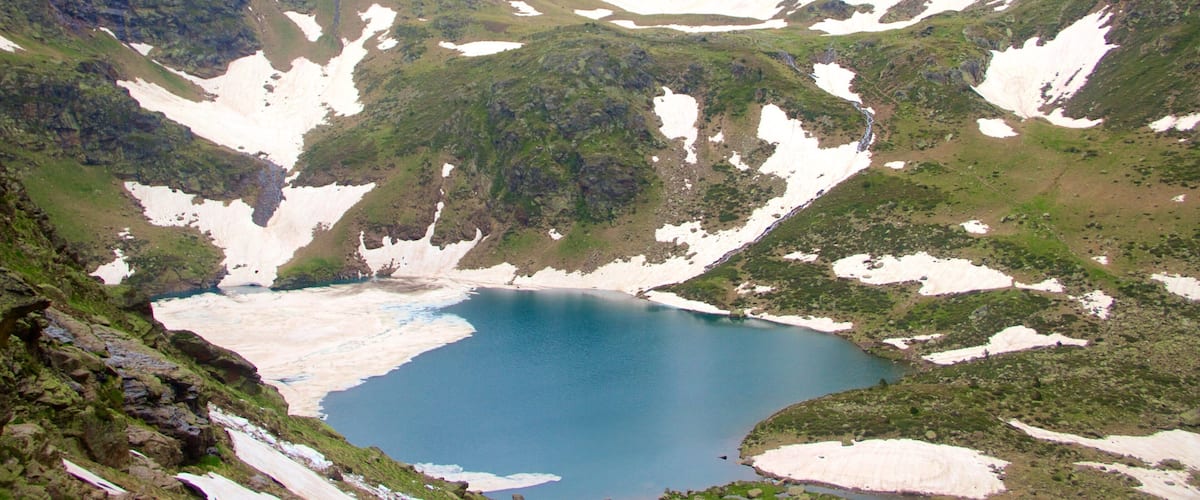 A glacial lake surrounded by rugged mountains with patches of snow and greenery.