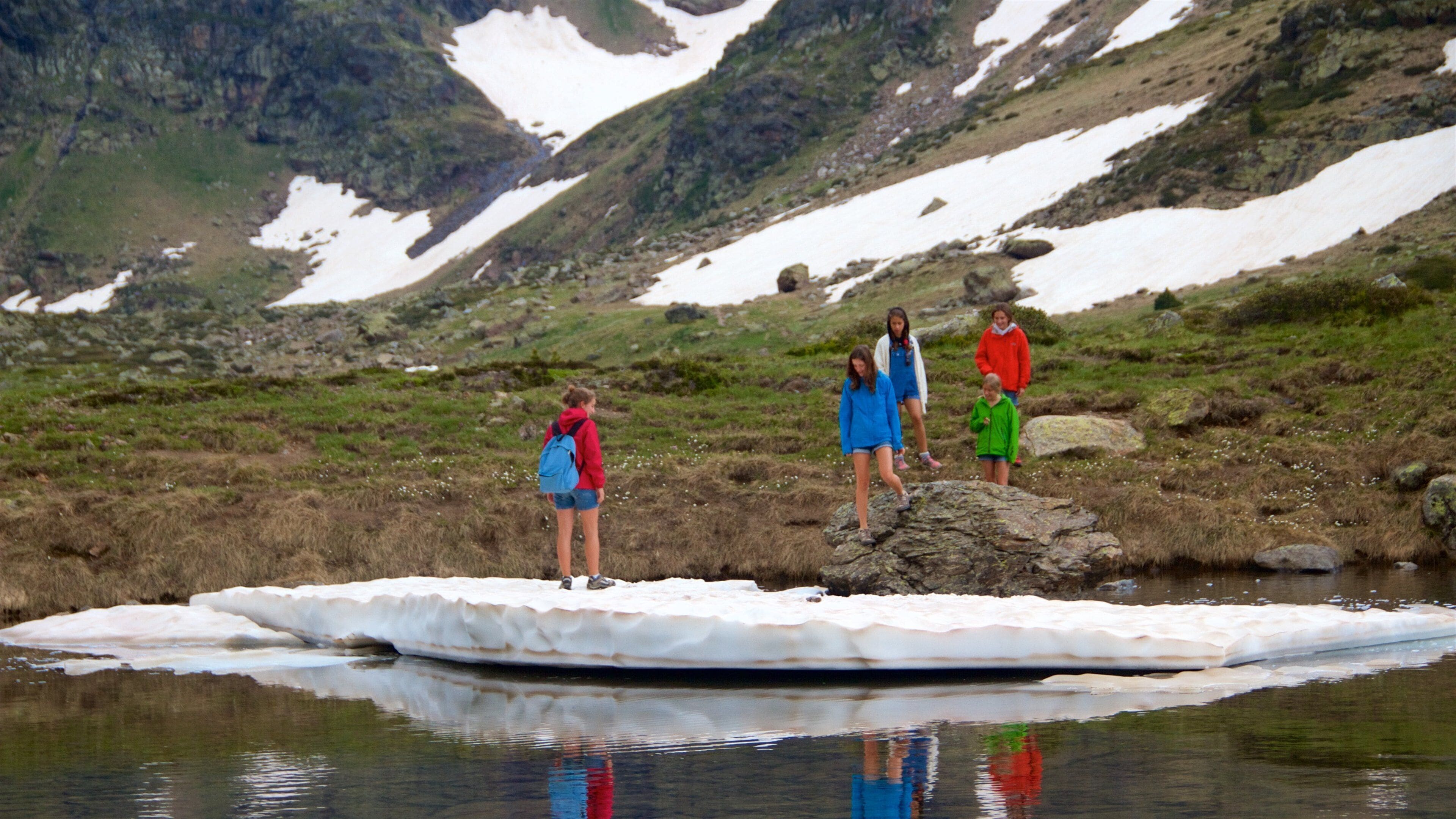 Un grupo de personas sobre un bloque de hielo flotante en una zona montañosa con parches de nieve.