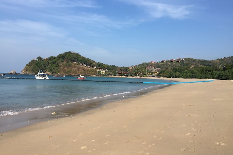 A beach with footprints, a boat, and houses on a hill.