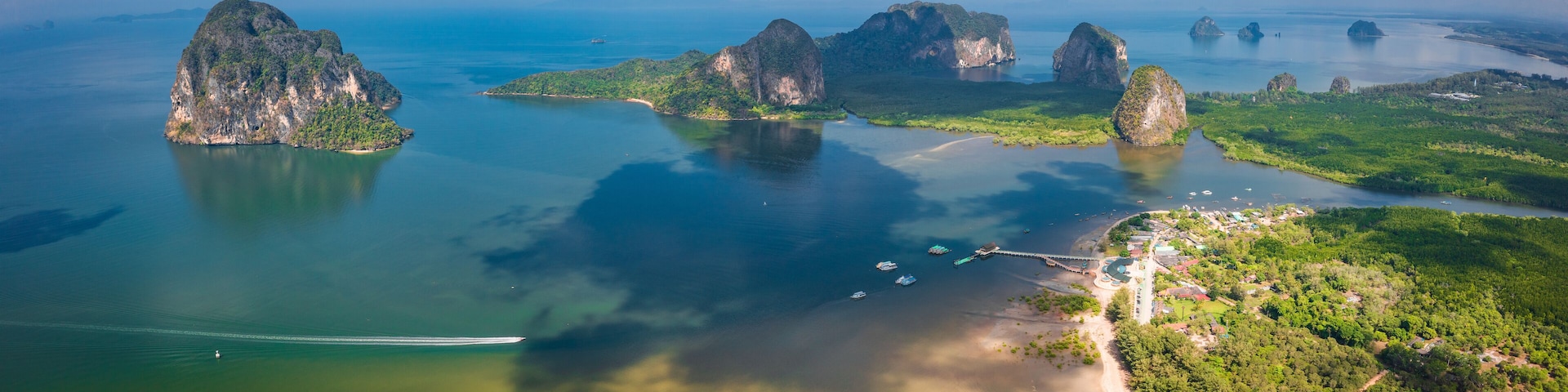 Un paisaje costero con islas de piedra caliza, aguas cristalinas y un pequeño poblado con barcos.