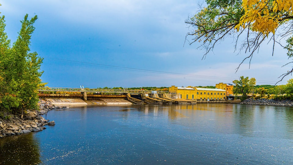 A river with a bridge, a dam, and buildings along the riverbank.