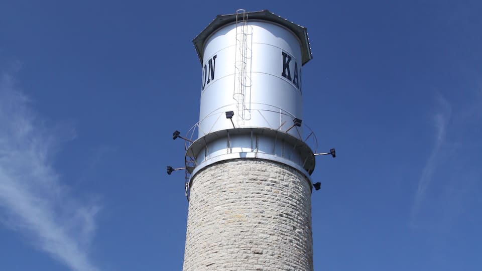 A tall stone lighthouse with a metal top against a clear blue sky.
