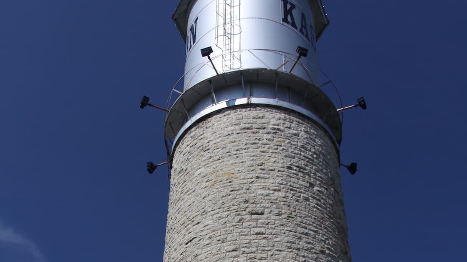 A tall stone lighthouse with a metal top and the letters "KAM" on it.
