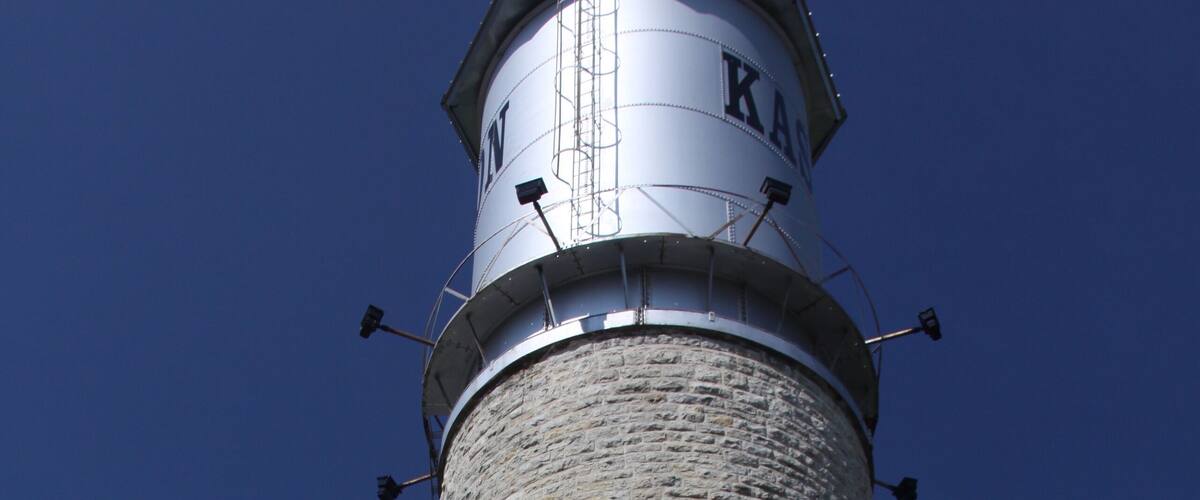 A tall stone lighthouse with a metal top and the letters "KAM" on it.