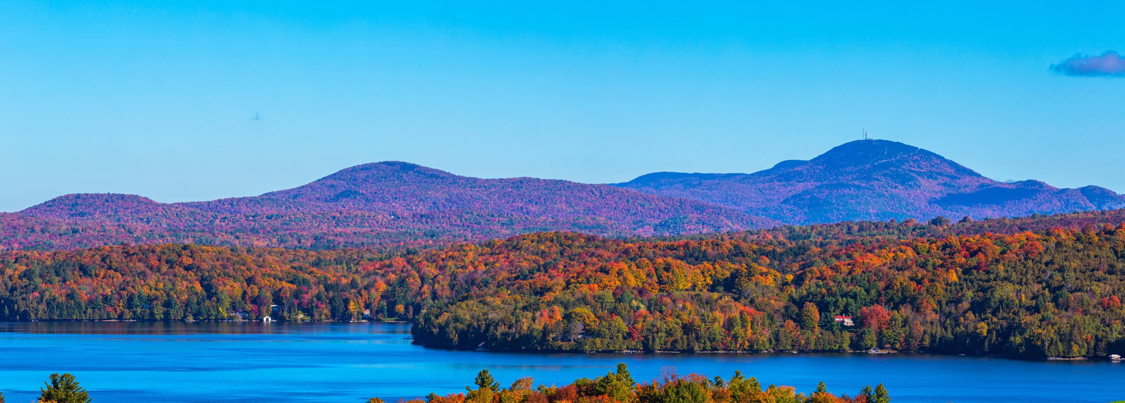 Un lac entouré de forêts aux couleurs automnales et de montagnes lointaines.
