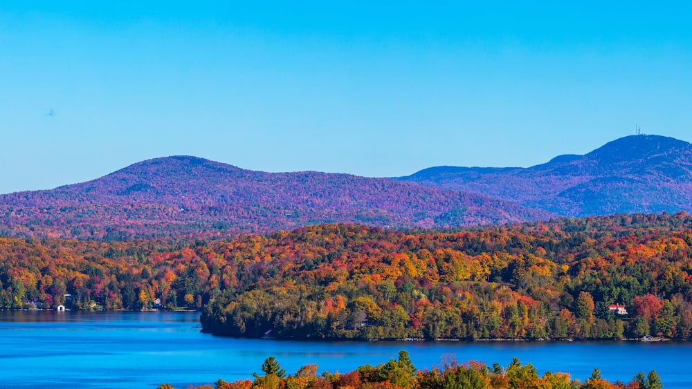 A lake surrounded by autumn-colored forests and distant mountains.