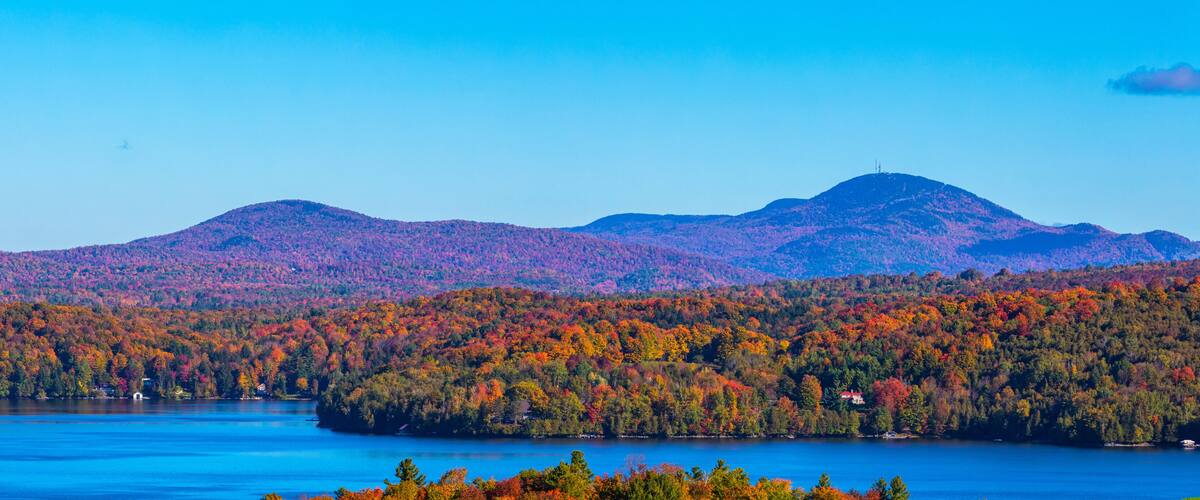 Un lac entouré de forêts aux couleurs automnales et de montagnes lointaines.